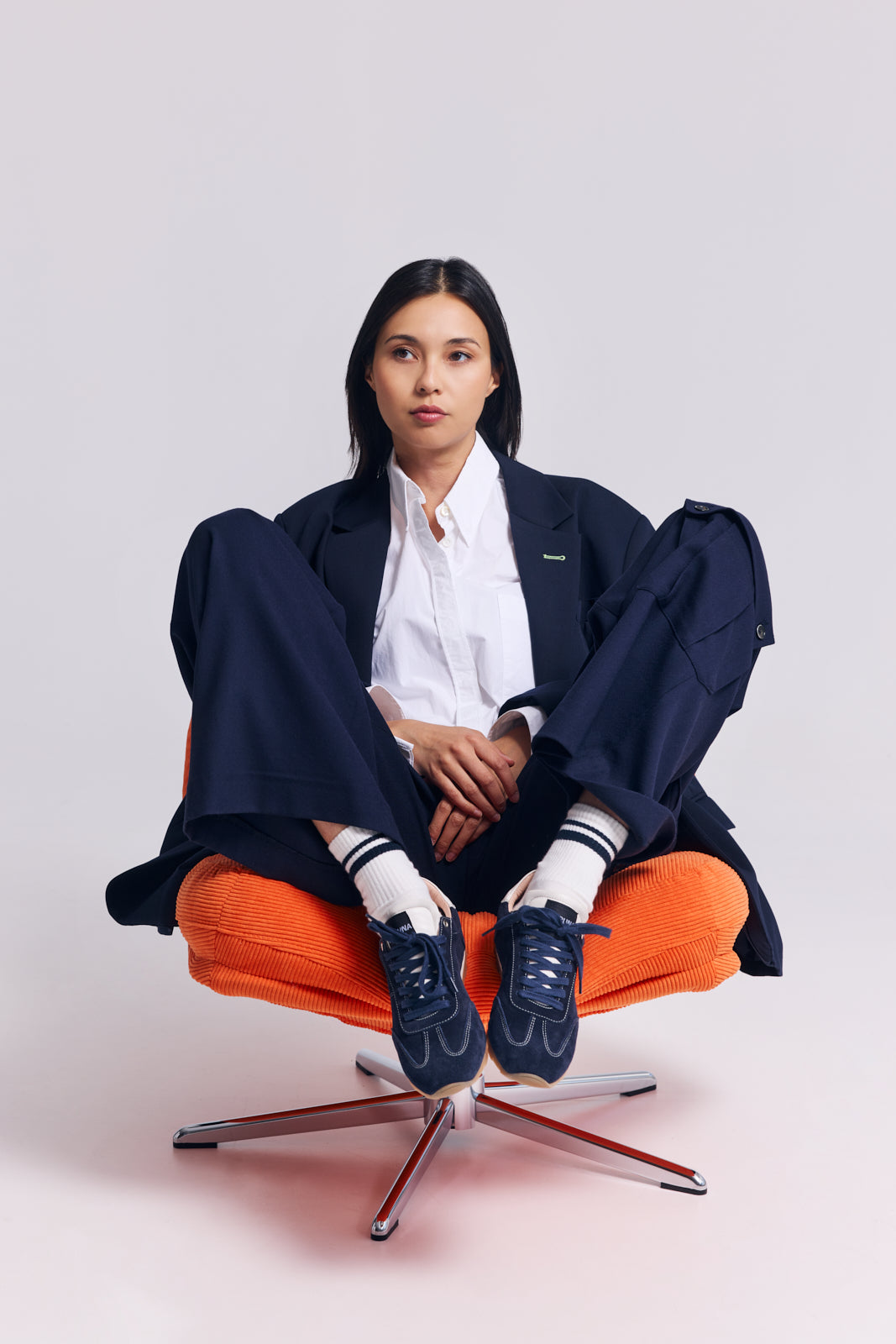 Person sitting on an orange chair wearing a navy outfit with white socks and blue shoes.