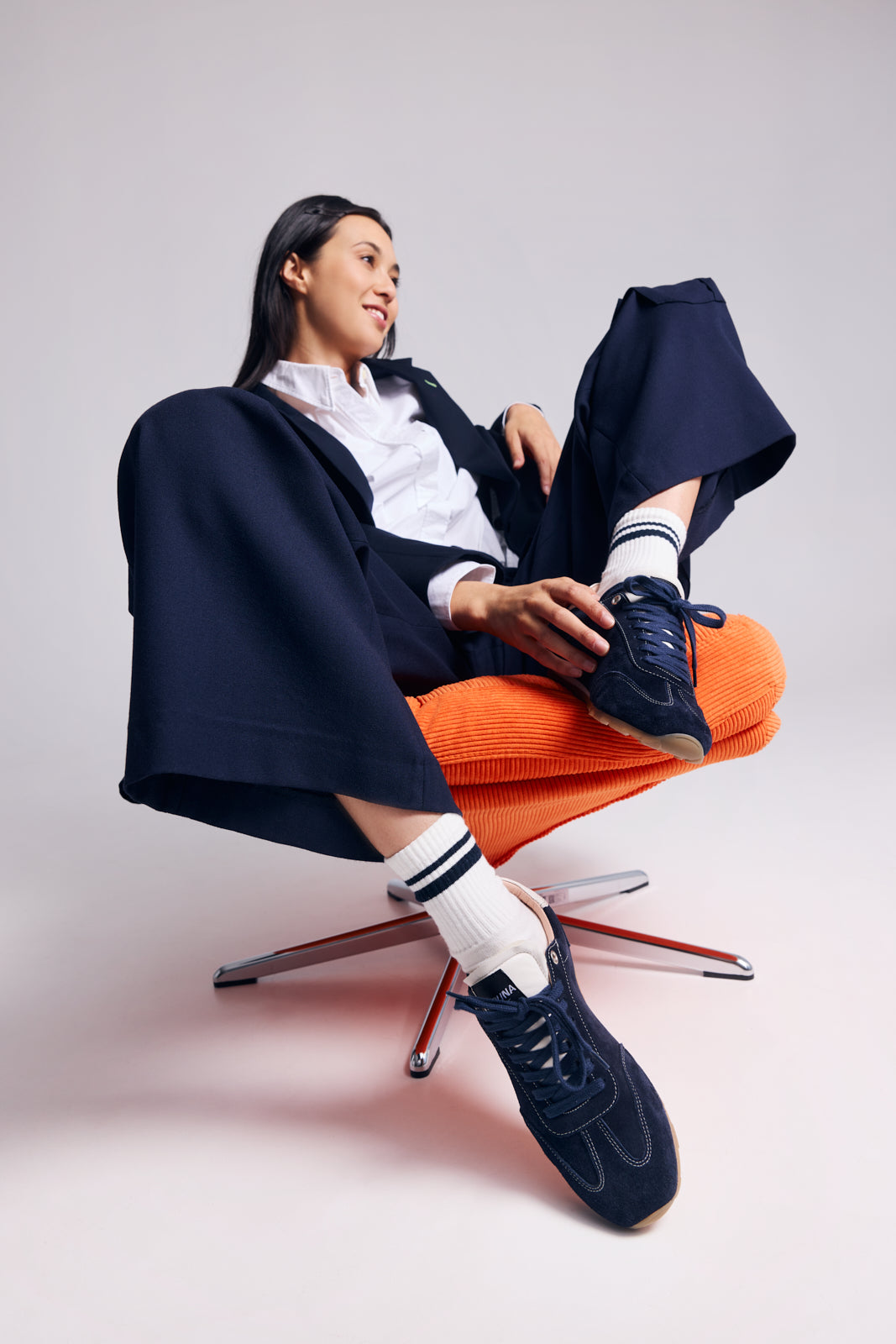 Person sitting on a chair wearing navy shoes, orange pants, and a navy coat.